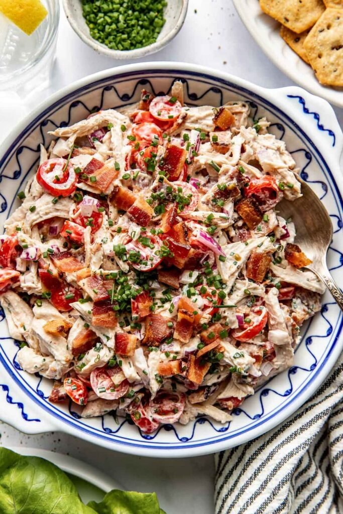 Overhead view of a bowl of BLT Chicken Salad topped with crisp bacon pieces and fresh chives.