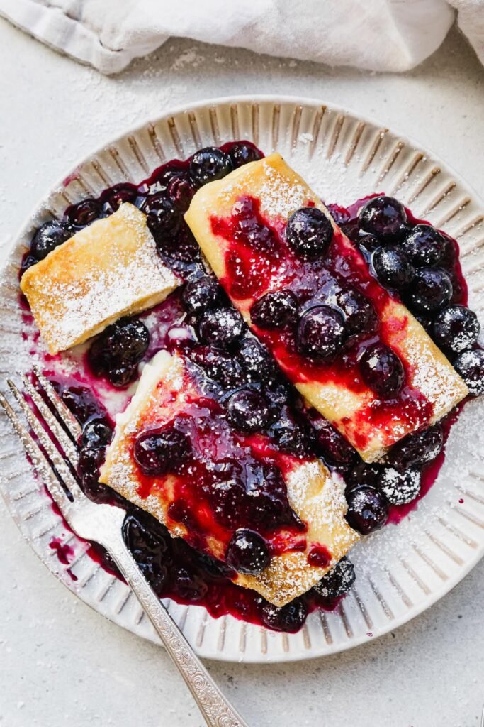 Cooked cheese blintzes on plate with blueberry sauce