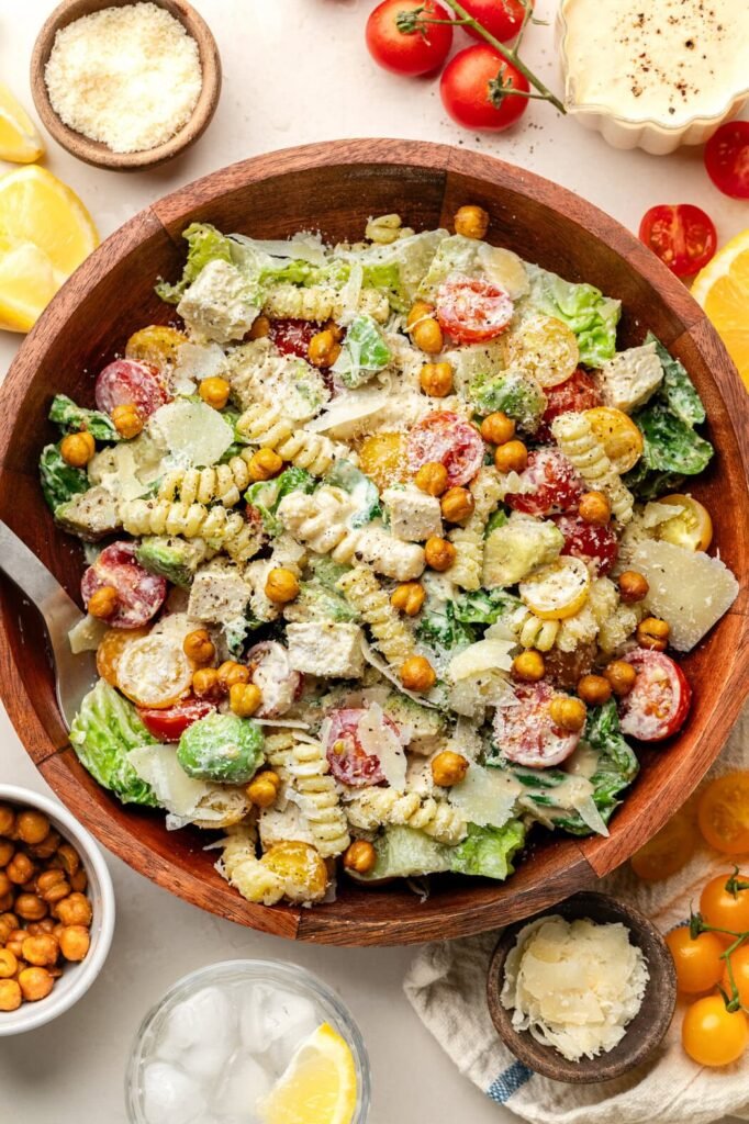 Overhead view of a wooden bowl filled with Chicken Caesar Pasta Salad topped with roasted chickpeas.