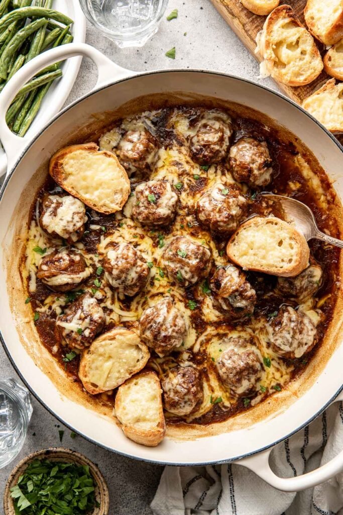 Overhead view of a skillet filled with French onion meatballs topped with cheese.