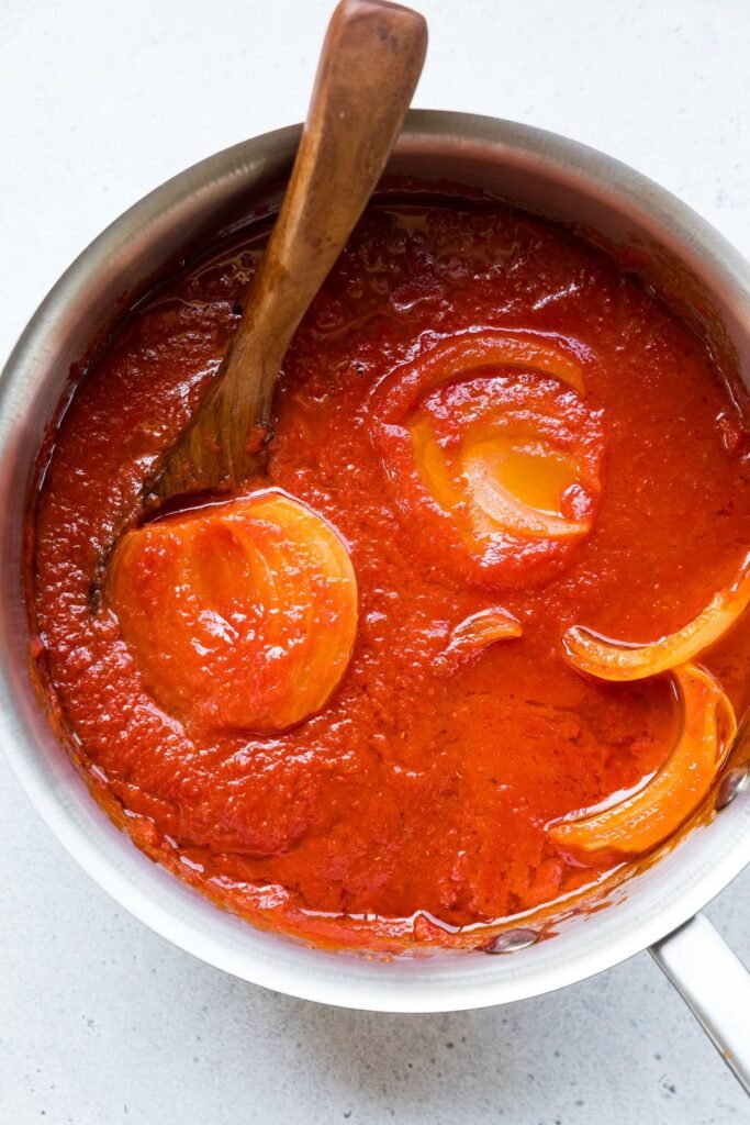 Lightened Marcella Hazan-inspired tomato sauce simmering in a pot with a halved onion