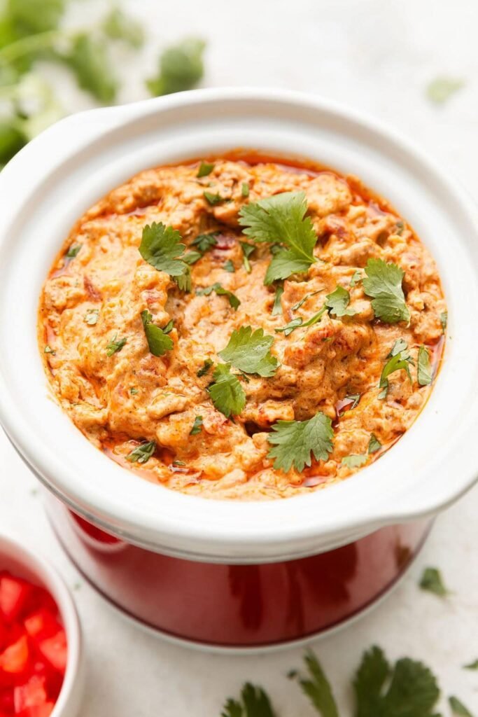 Close up view of a small slow cooker filled with Rotel Dip sprinkled with fresh cilantro.