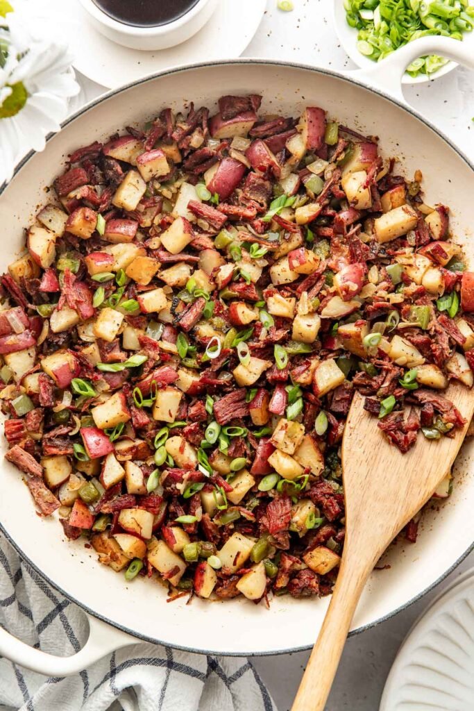 Overhead view of a white skillet filled with Corned Beef Hash topped with green onions.