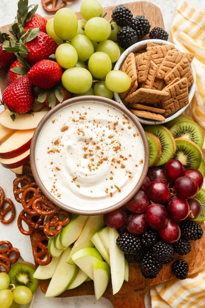 Overhead view of a variety of colorful fruit with a bowl of creamy fruit dip in the middle sprinkled with cinnamon.