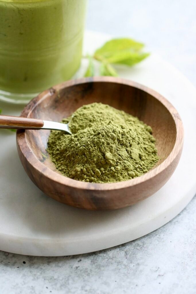 Close up view of a small wooden dish filled with green matcha powder with a spoon stuck into the powder.