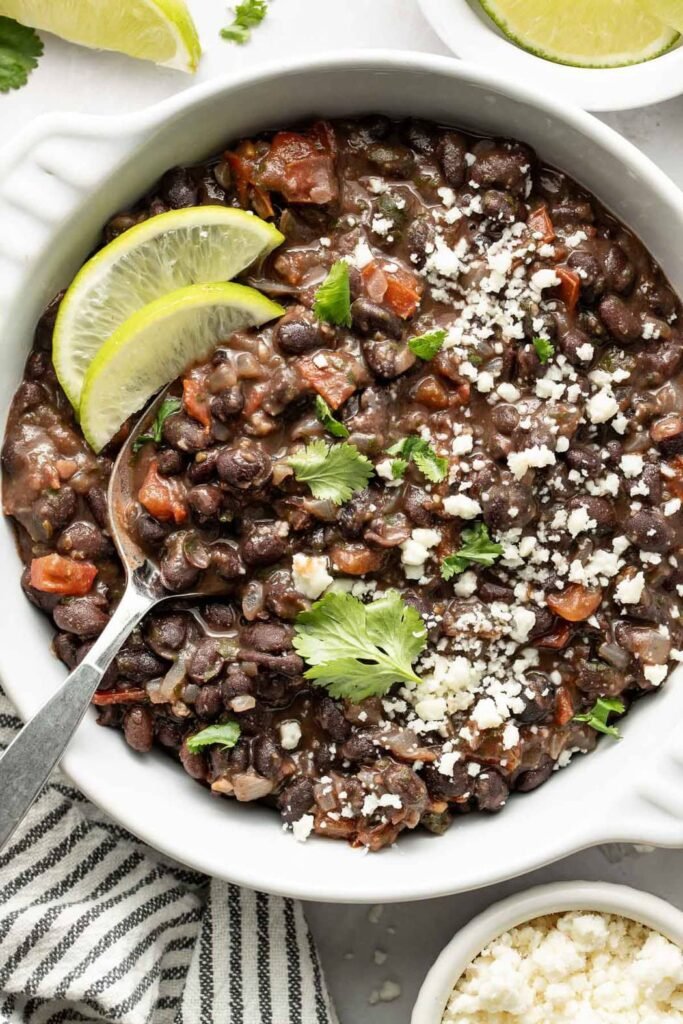 Overhead view of a bowl of Mexican Black Beans topped with fresh cilantro and garnished with lime wedges.