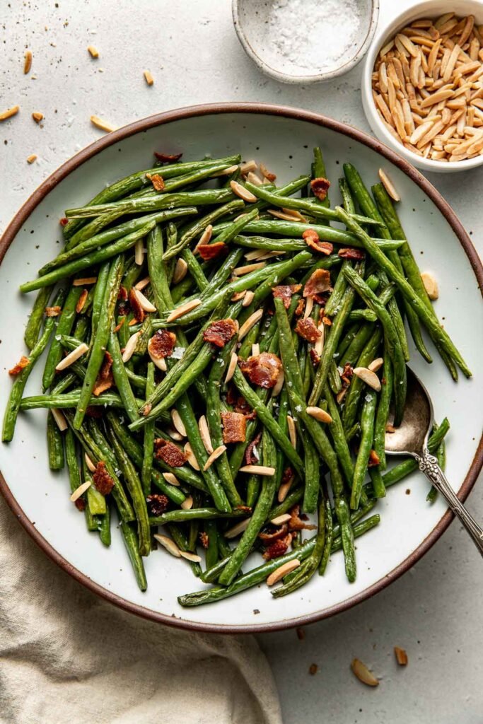 Overhead view of a plate of Roasted Green Beans topped with bacon pieces and slivered almonds.