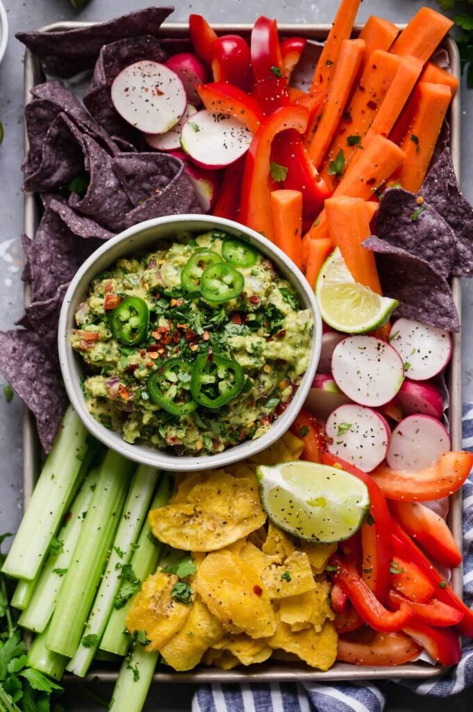 Overhead view of a bowl of fresh guacamole surrounded by freshly cut colorful veggies.