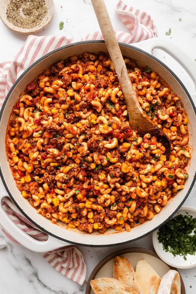 Overhead view of a skillet filled with goulash topped with fresh herbs and a wooden spoon stuck in the side.