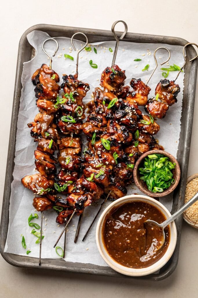 Overhead view of a sheet pan of Korean BBQ chicken skewers topped with green onions and sesame seeds.