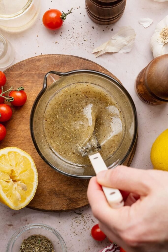 Overhead view of a hand stirring an Italian Dressing mixture in a measuring glass.