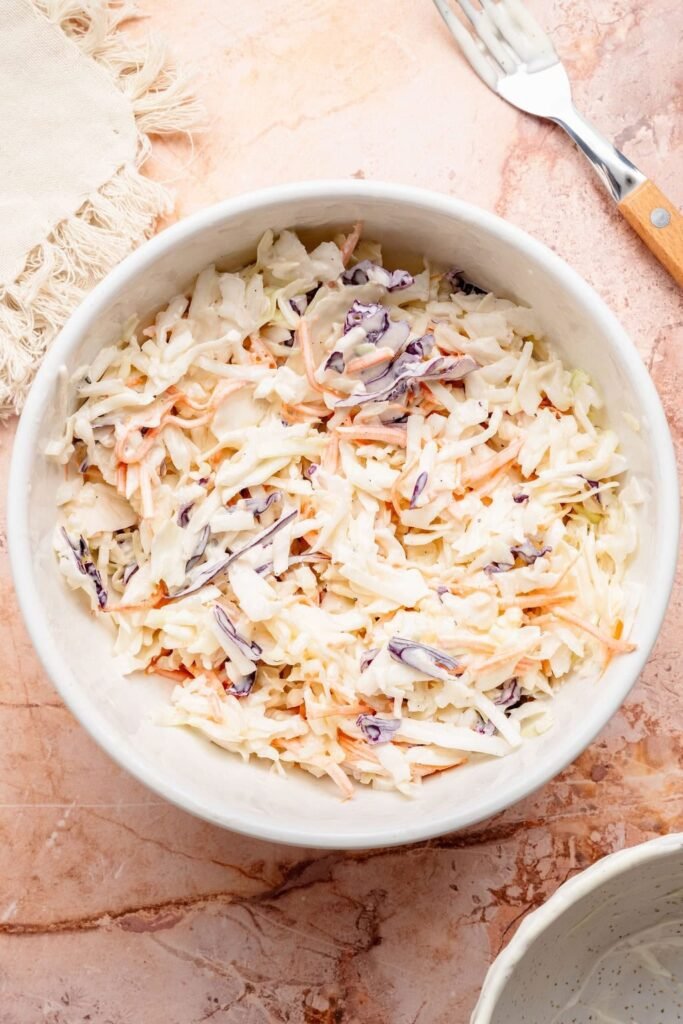 Overhead view of a white bowl filled with fresh coleslaw.