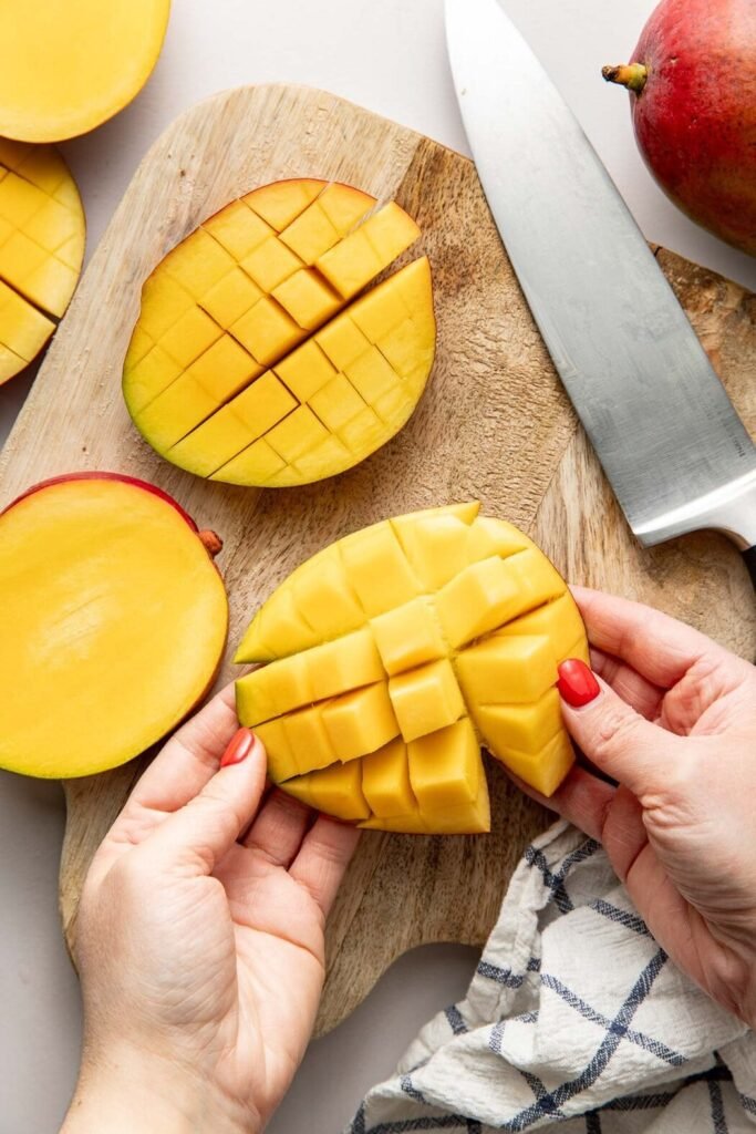 Overhead view of hands gently inverting a mango cheek so square shaped pieces pop forward.
